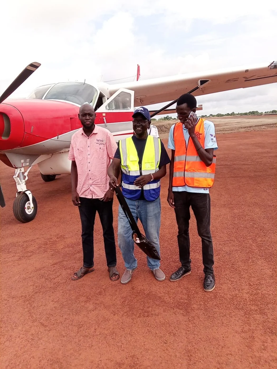 Delmark field staff standing beside a red-and-white aircraft on an airstrip